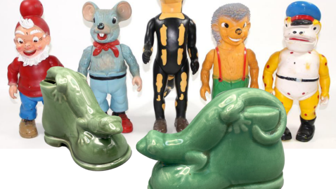 Eine Gruppe von sechs farbenfrohen Vintage-Reklamefiguren, darunter ein Zwerg, oder Gnom, Lurchi die Eidechse, eine Maus, ein Igel und ein Pilot, steht hinter zwei seltenen, grünen Keramik-Spardosen von Salamander in Lurch-Form.