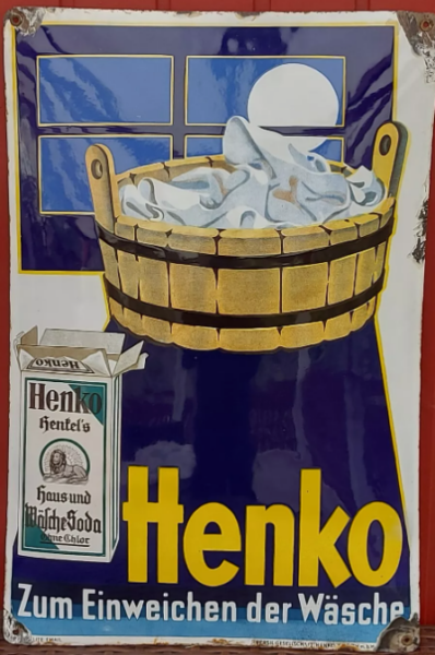 Eine alte Henko-Werbung zeigt einen mit Seifenlauge gefuellten Waeschezuber unter einem vom Vollmond beleuchteten Fenster. Links auf der Henko-Waschmittelpackung steht deutscher Text, darunter steht in fetter gelber Schrift Henko Zum Einweichen der Waesche.