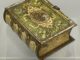 Eine Vintage-Metalldose im Buchdesign auf transparentem Boden. Die Dose hat einen goldenen Buchrücken mit geprägtem Text und einen verzierten grünen Deckel mit dem russischen Doppeladler und floralen Mustern. Die Blechdose weist Gebrauchsspuren auf.