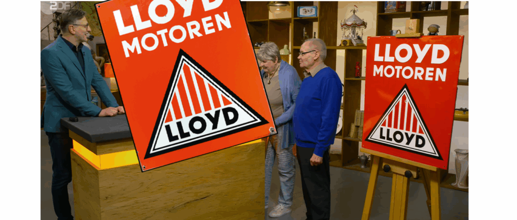 Drei Personen stehen in einem Studio mit Regalen und Antiquitäten, zwei halten ein großes rotes Lloyd-Emailschild mit der Aufschrift "LLOYD MOTOREN". Im Vordergrund ist eine vergrößerte Version geschnitten - eine klassische Bares für Rares-Szene mit einem restaurierten Vintage-Artikel.
