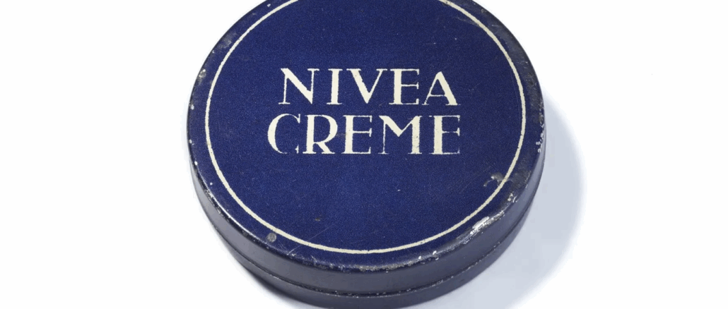 Eine runde, dunkelblaue Dose mit weißem Rand und dem Text "NIVEA CREME" in fetten weißen Großbuchstaben auf dem Deckel. Diese ikonische Dose stammt von 1925.