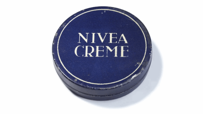 Eine runde, dunkelblaue Dose mit weißem Rand und dem Text "NIVEA CREME" in fetten weißen Großbuchstaben auf dem Deckel. Diese ikonische Dose stammt von 1925.
